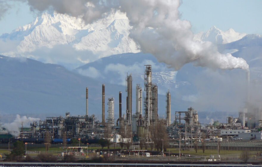 Oil refinery with distillation towers and steam against mountains